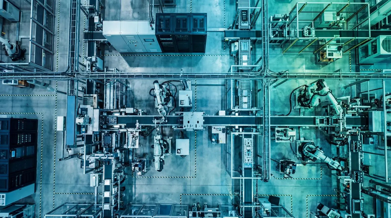 Overhead view of a manufacturing factory floor with robotic arms, PLCs, and OT devices illustrating AI vulnerability discovery risks in unpatchable industrial systems