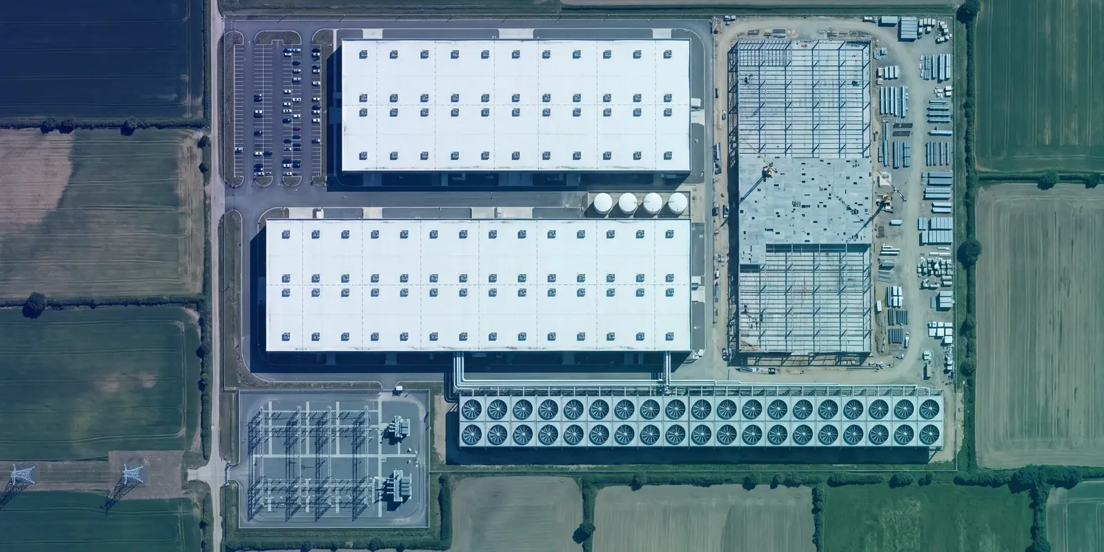 Overhead aerial of a data center campus under construction in farmland, illustrating AI agent containment architecture