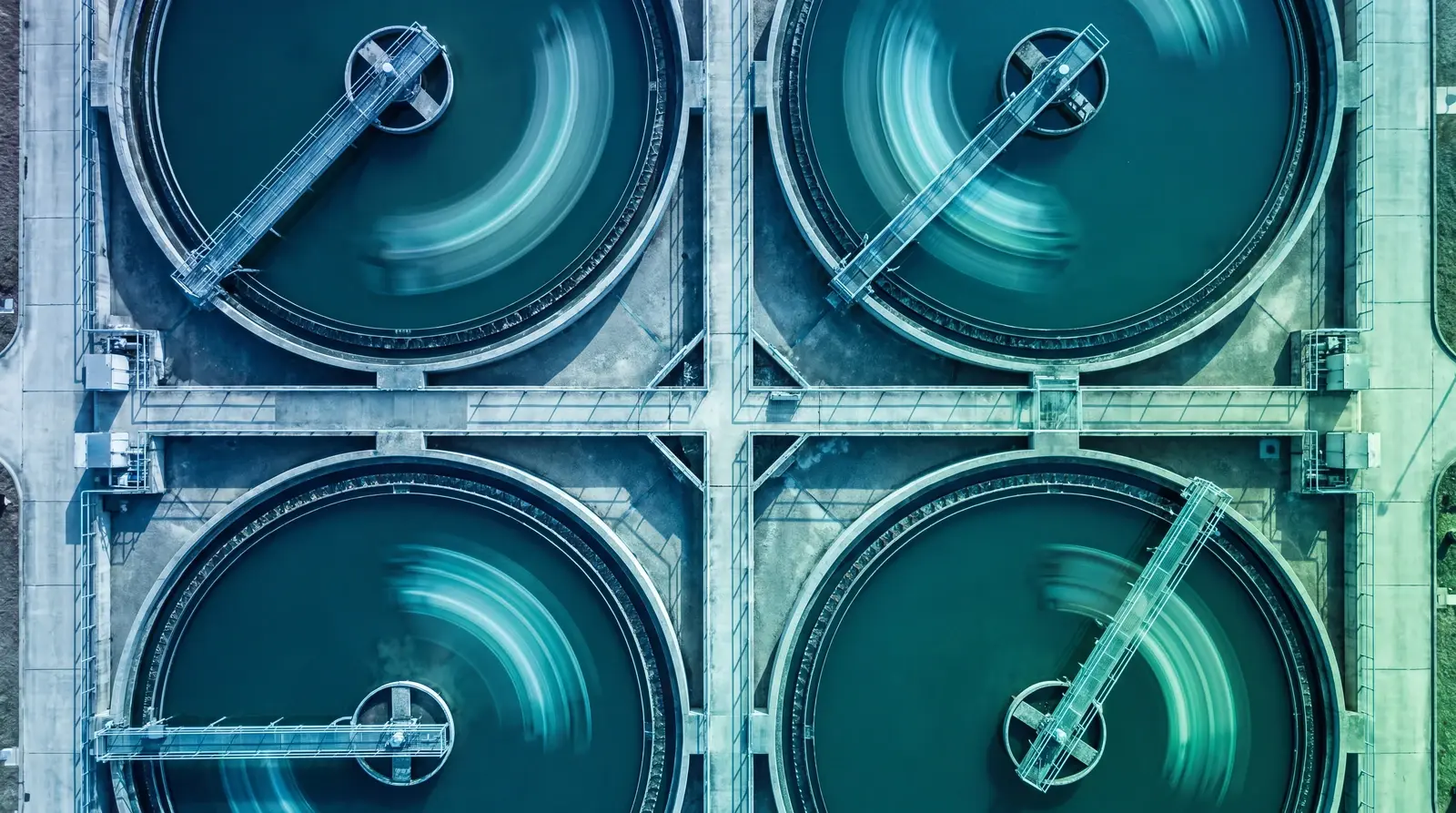 Clarifier basins from above, skimmer arms blurred mid-sweep, a metaphor for continuous least privilege enforcement for AI agents