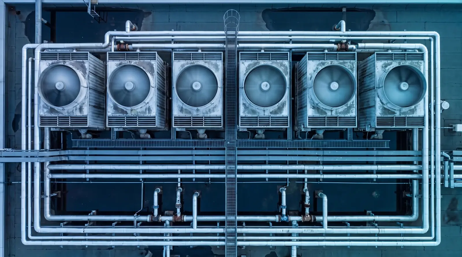 Overhead view of a hospital central utility plant deck: six cooling-tower fans and the pipe rack they hang off.